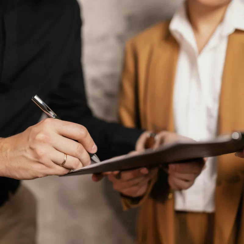 Man signing document on a clipboard with a legal professional in the background