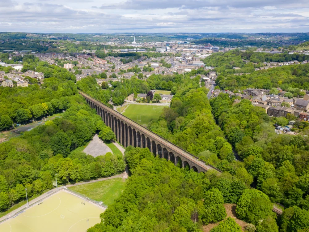 An aerial photo of Lockwood viaduct, Huddersfield, surrounded by trees and with the town in the distance.